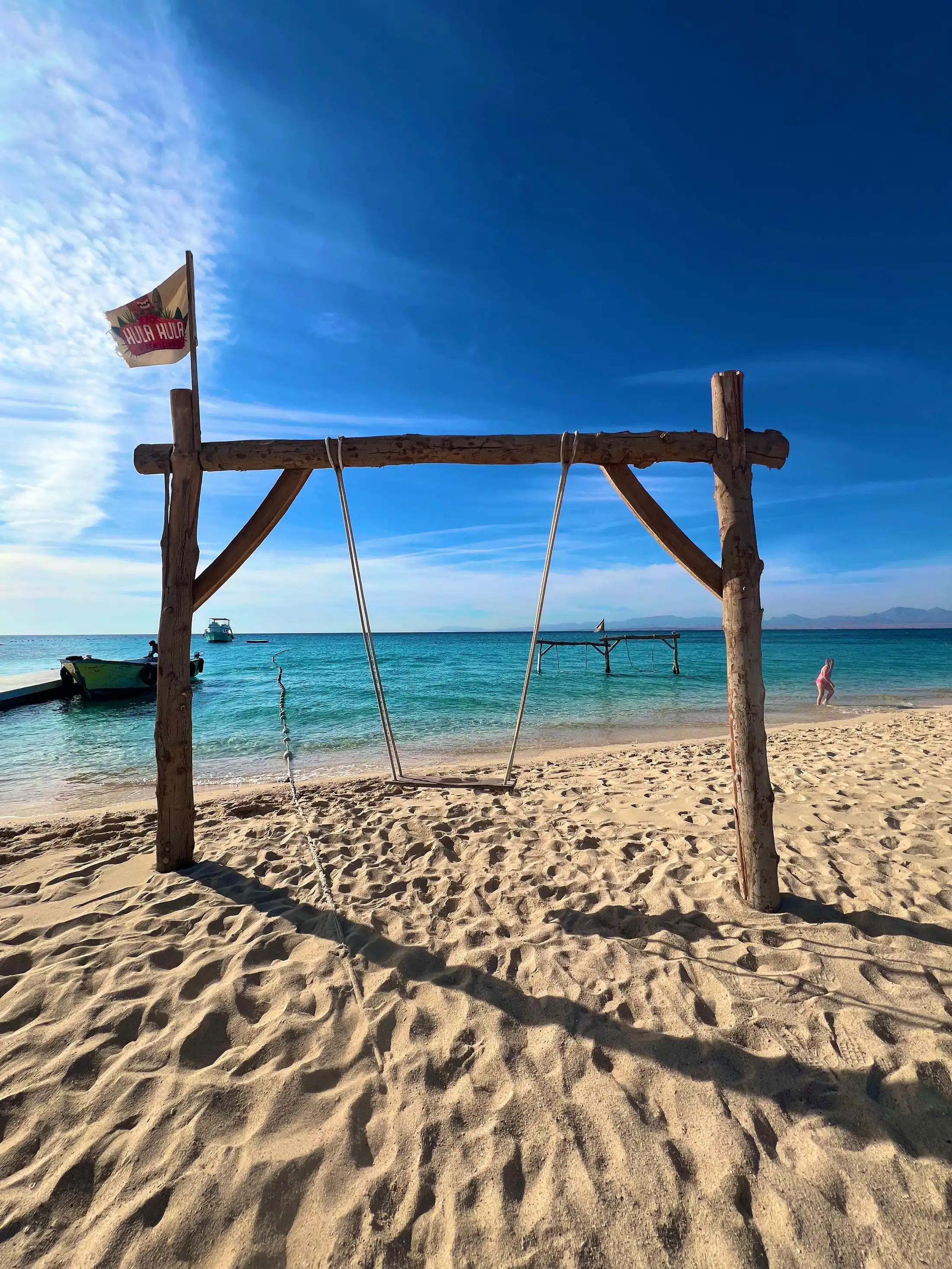 Beach swing by the turquoise sea at Hula Hula Island with excursion boats in the background